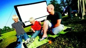 Förväntansfulla. Viktor och Carl stojar i solen tillsammans med pappa Roger Davidsson. I bakgrunden syns den väl tilltagna bioduken där filmen "Göta kanal 2 - kanalkampen" senare visas. Foto: Ellen Kindstrand