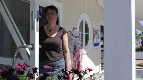 Mariette Eskilsson välkomnar till sin nya klädbutik i Loftahammar, bakom skymtar lite av de kläderna som Mariette säljer. Butiken ligger i det gamla bankhuset och ska hålla öppet augusti ut. Foto: Frida Andersson