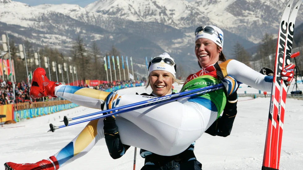 Klassiskt foto där Anna Olsson lyfter upp Lina Andersson efter att Andersson säkrat OS-guldet i Turin 2006. Det första svenska OS-guldet på damsidan i längdskidåkning sedan OS 1968 i Grenoble.