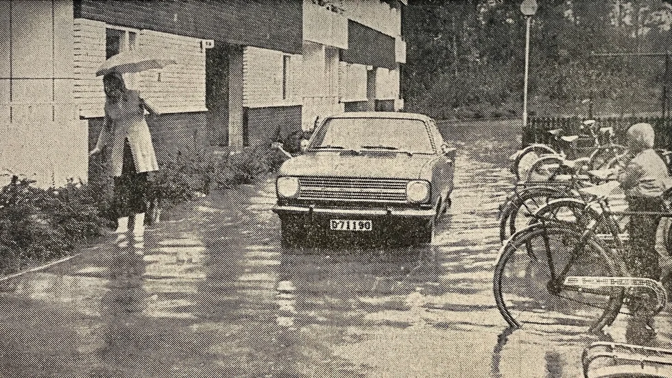 Kuriren för 50 år sedan: Eva Eng vadar ut från Halvergatan 9B med paraply i den ena handen och en genomsur schäfervalp i den andra. Säkrast var det nog att ta sig fram med bil i det aktuella området. Vattnet stod decimeterhögt utanför Halvergatan 9B. 