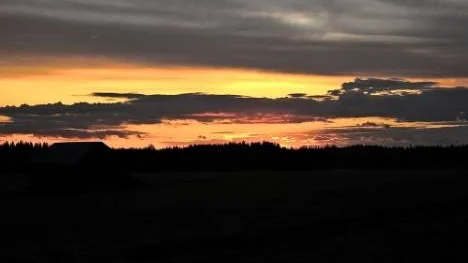 Stannar bilen på midsommarnatten och ser en vacker, orange himmel.