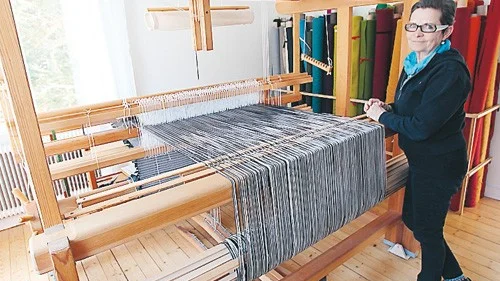 Karin Sjögren hemma vid sin gigantiska vävstol. I bakgrunden står alla hennes rullar med tovad ull.