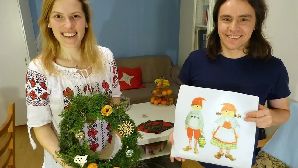 Luiza Timoc och Alin Mechenici har bott i Sverige några år och berättar om jultraditioner i födelselandet Rumänien. Här håller Alin en svensk julteckning medan Luiza visar en julkrans hon gjort. Foto: Leif Larsson
