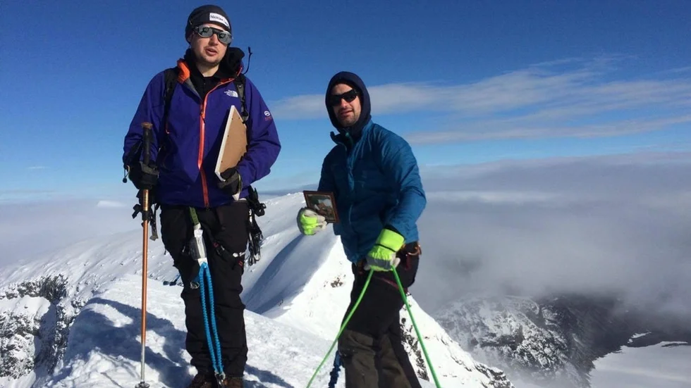 Nicklas Lautakoski och Christoffer Andersson på Kebnekaises topp, med en bild på sin vän. Solen bröt igenom molnen precis när de nådde toppen.