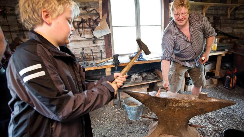 Smeden Erik Berglund får hjälp av unge Adam Björkén med att hamra och forma den rödglödgade delen av järnet.