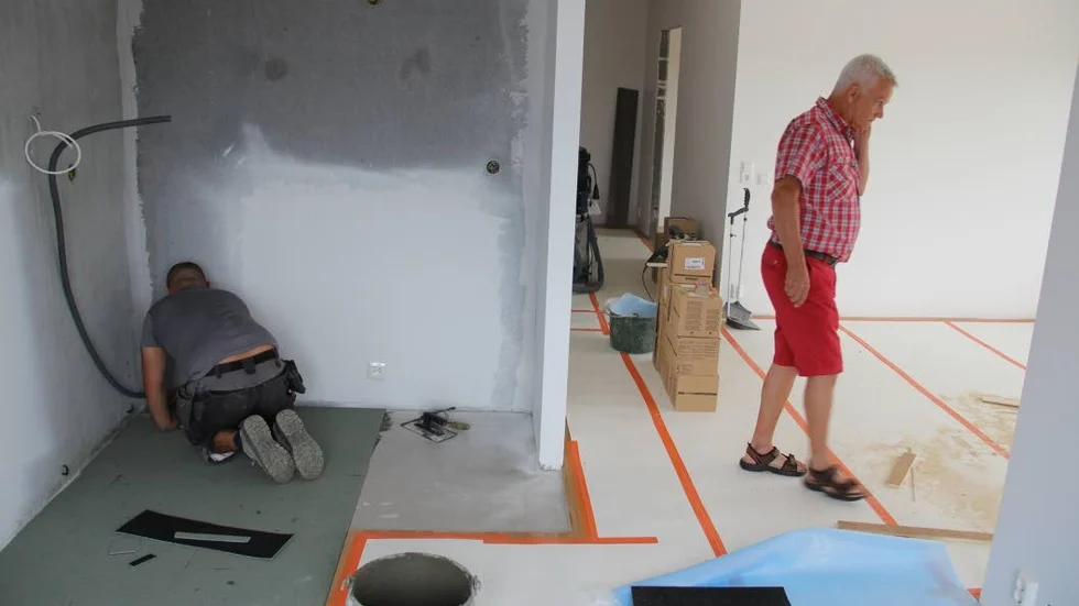 Golvläggning. En byggnadsarbetare ljudisolerar i köket där det ska ligga klinker i Tierpsbyggens nya hyreshus vid Badhusgatan i Tierp. Till höger projektledaren Bengt Persson.