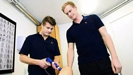 Naprapatstudenterna Kristoffer Weckström och Johan Söderström behandlar en knäled med stötvågsbehandling.