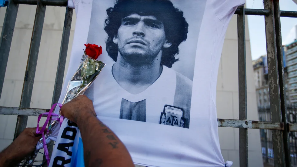 En man hänger en ros på en t-shirt föreställande Diego Maradona i samband men en protestmarsch i Buenos Aires i mars 2021. Många kräver fortsatt svar på om allt gick rätt till i samband med fotbollslegendarens död. Arkivbild.