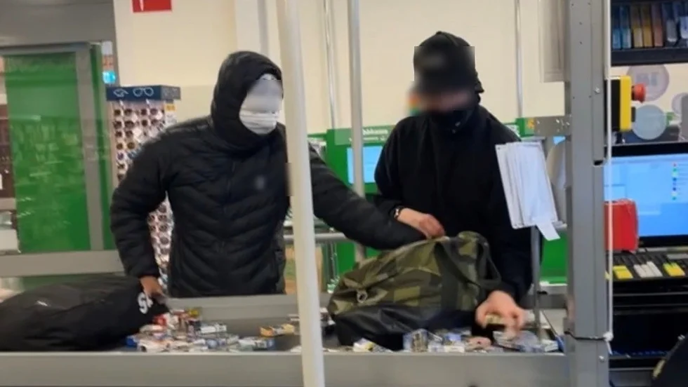 Bilden är tagen av ett vittne som röt ifrån mot rånarna och skrämde åtminstone en av dem på flykt. Vittnet beskriver dem som unga killar. Här samlar de ihop cigarettpaket som personalen lagt upp på disken på deras uppmaning.