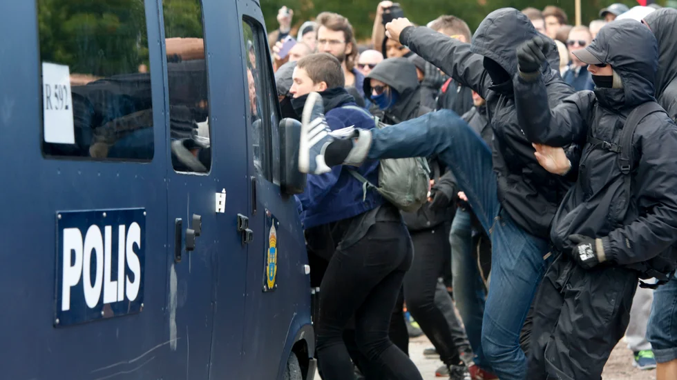 Maskerade motdemonstranter sparkar på polisbil och springer iväg under Svenskarnas partis torgmöte i Malmö på lördagen. Foto: Drago Prvulovic/TT