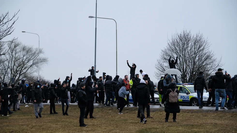 Individer står uppe på polisbilar och ett stort antal personer befinner sig runt fordonen.