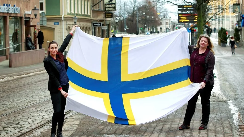 Snart premiärvisning. Snart kommer den här flaggan för första gången att hissas på Saltängsbron. Den nya officiella Sverigefinska flaggan, som här visas upp av praktikanten Nadia Bednarek, till vänster och Raija Arvidsson, samordnare för Finskt förvaltningsområde hos Norrköpings kommun.