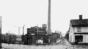 Så här mycket mer småskaligt såg det ut före de stora ny- och tillbyggnader som längre fram i tiden skulle ske länge Bredgatan, för både Campus och annat. Men här är året 1928 och Kåkenhusbyggnaden var en del av Yfa-textilen, där också det lilla färgeriet som låg bakom planket ingick. På affischtavlan, som tillhörde Östergötlands Dagblad, gör en filmaffisch reklam för Gyllenbom smiter iväg till utlandet. Invid läser vi något om jazzmusik men kan inte urskilja vad där mer står. I byggnaden till höger hann butikerna avlösa varandra genom årtiondena. Under ett antal år framåt återfanns här den bandageaffär, som (läser vi) innehades av Oskar Ekmans eftr. Fotograf var Karl Lindelöw, och originalfotografiet återfinns i Stadsarkivets samlingar.