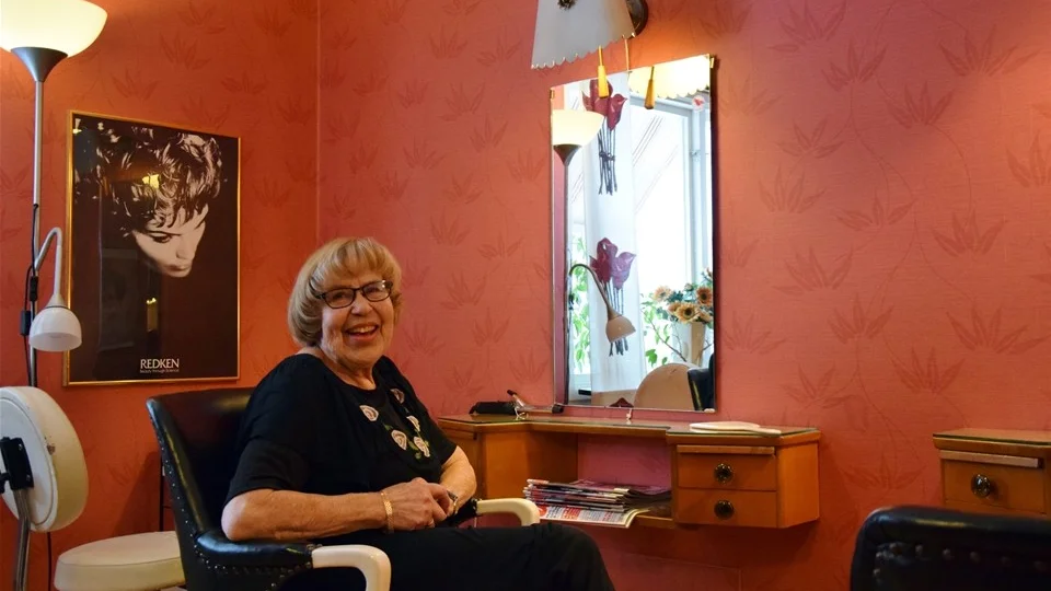 Ulla Brissle sitter i sin charmiga salong med lampor och hyllor från 30 talet och stolar med gängad stång. Foto: Morgan Karlsson