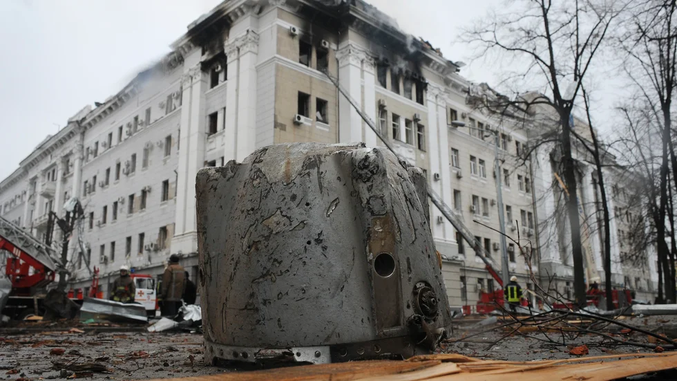 Rester från en raket ligger på gatan i Charkiv. I bakgrunden ses Ukrainas säkerhetstjänsts skadade byggnad under onsdagen.