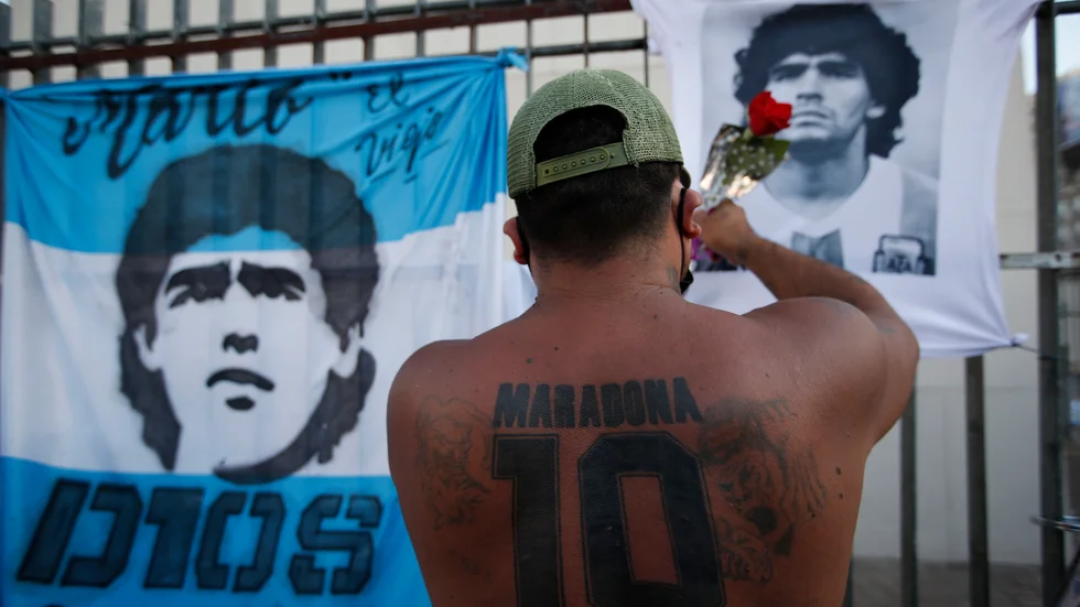 En fotbollssupporter i Buenos Aires hänger en ros på en t-shirt föreställande Diego Maradona, som dog i november förra året. Arkivbild.