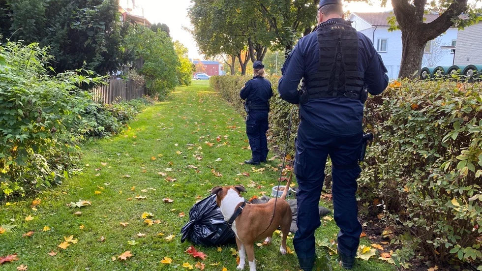 Poliser står utanför lägenheten med en hund som påträffades i lägenheten. Hunden har omhändertagits av polispatrull.