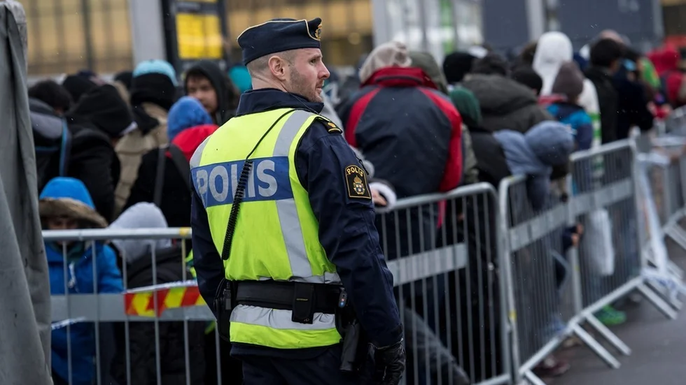 MALMÖ 2015-11-19 
En polis övervakar kön av ankommande flyktingar i snålblåsten vid Hyllie station utanför Malmö på torsdagseftermiddagen. Alla som saknar id-handlingar får sedan Sverige införde inre gränskontroller kliva av tågen som anländer från Danmark vid station Hyllie. De som söker asyl bussas vidare till Migrationsverket, övriga får åka tåg tillbaka till Danmark. Regeringen har förlängt den tillfälliga gränskontrollen i Sverige med tre veckor, till den 11 december. Samtidigt slår Migrationsverket larm om att alla registrerade asylsökande inte längre kan erbjudas boende. 
Foto: Johan Nilsson / TT / Kod 50090