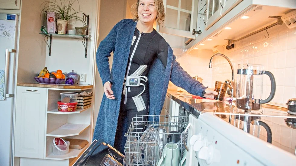 Jennie Granat plockar i diskmaskinen, samtidigt som hon använder dräkten, hemma i sitt kök i Nyköping.