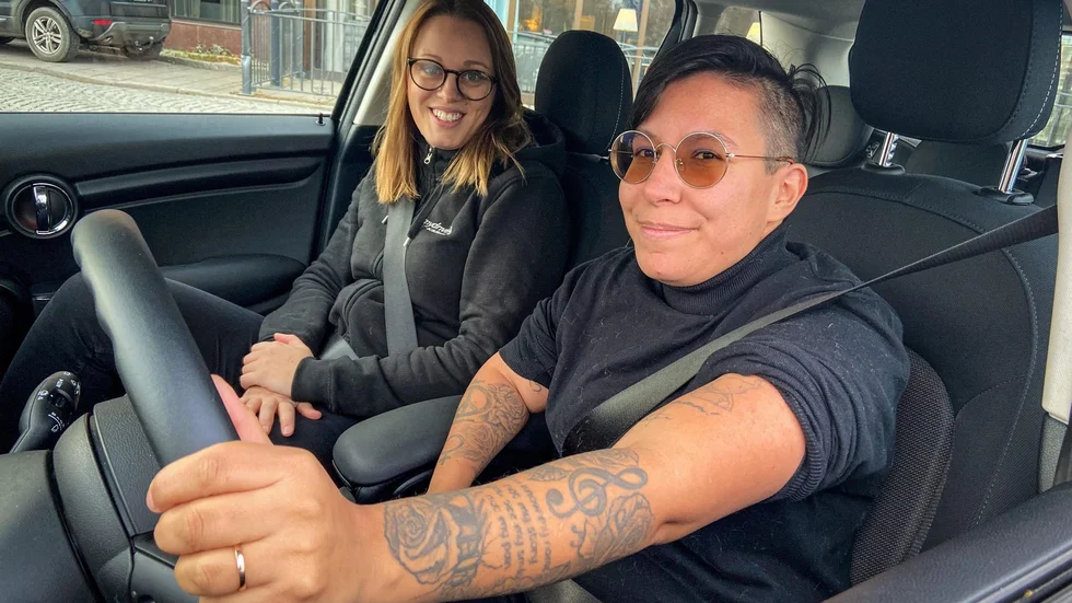 Carro Anttila vid ratten bredvid körskolläraren Hanna Dovsten. På insidan av vänster arm har Carro låtit tatuera in en hylling till sin körskollärare.