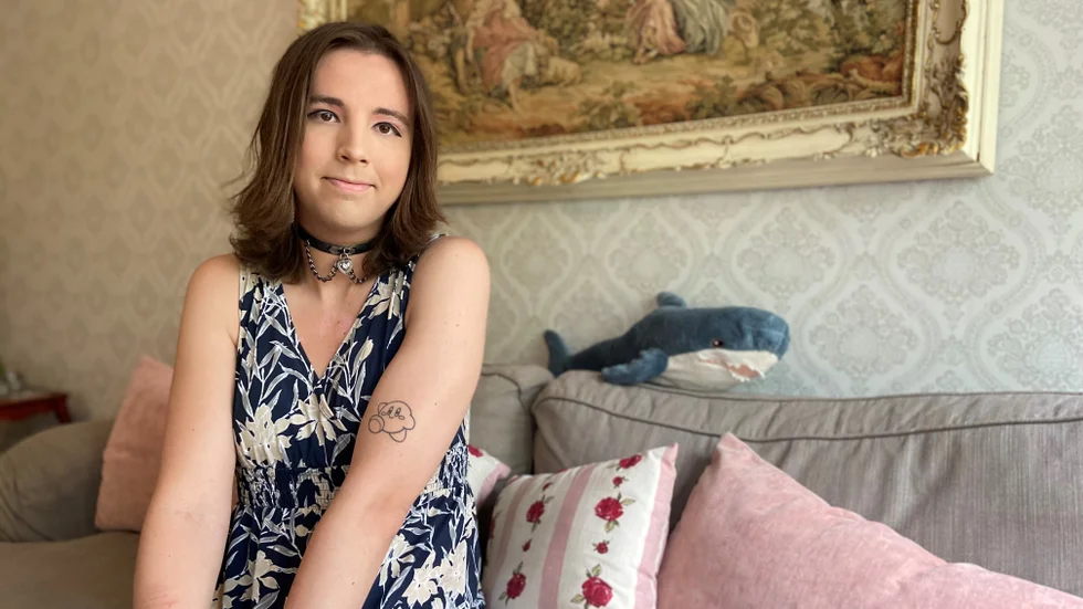 Dina Millertson i soffan som pryds av en mjukishaj. Den har blivit något av en maskot för transrörelsen eftersom den har transfärgerna, blått, rosa och vitt.