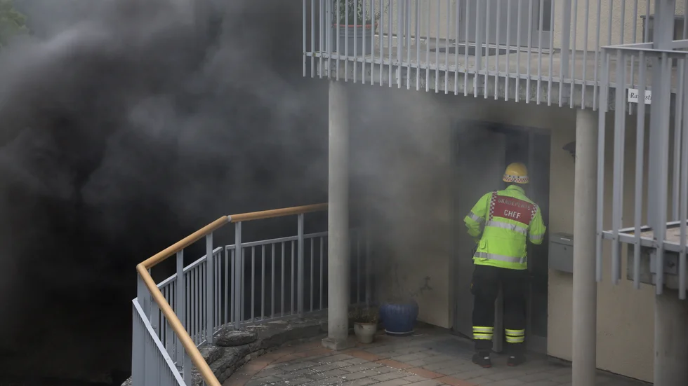 Skadechefen tittar in i en lägenhet medan svart rök bolmar ut ur ventilationsanläggningen.