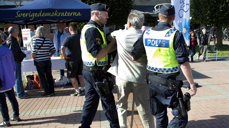 Miljöpartisten Rune Tessin avhystes av polis från Sverigedemokraternas torgmöte.
