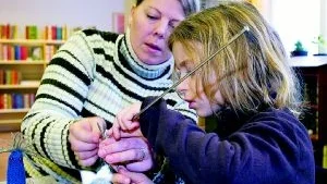 Bibliotekarien Carina Zandelin hjälper Elsa Wernmarker, 7, med stickningen, i samband med att Skärblacka bibliotek igår anordnade stickningsutbildning för de sportlovslediga som ville prova på detta hantverk. På bilden syns också ett par av de små stickade fingerdockorna. Foto: Anita Kjellberg