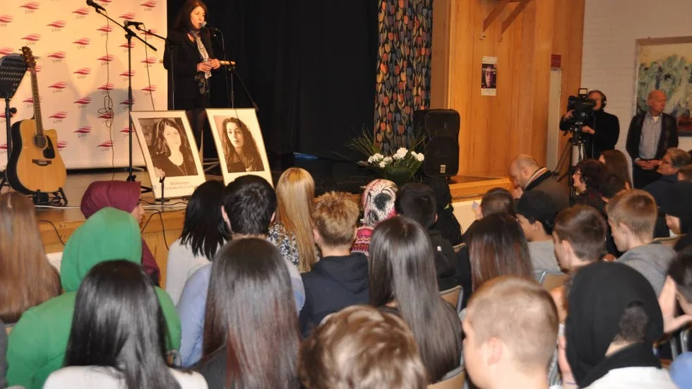 Konferenciern Sara Mohammad i skolans aula. Framför henne porträttbilder på Pela och Fadime.