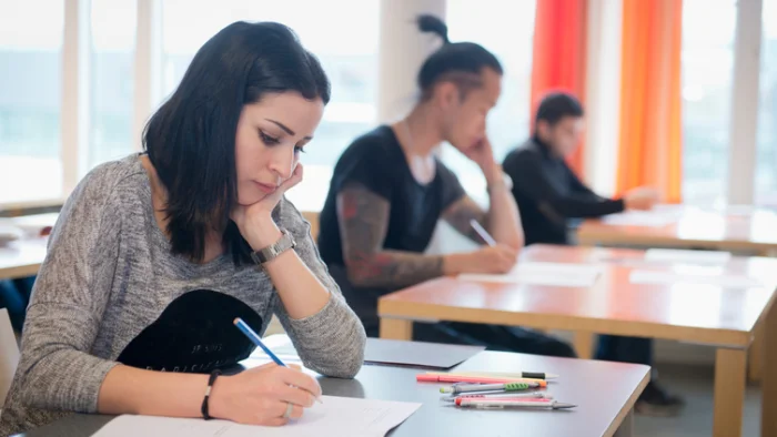 Tre studenter skriver högskoleprovet i skolsal.