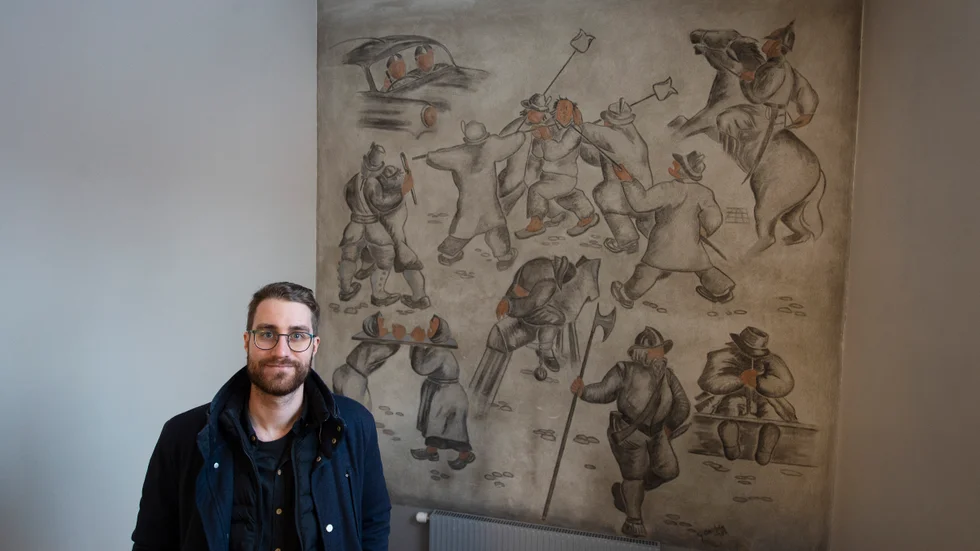 Christopher Wisting vid kommunens mark- och exploateringsenhet, ståendes framför en av de gamla väggmålningarna som finns i trapphusen.