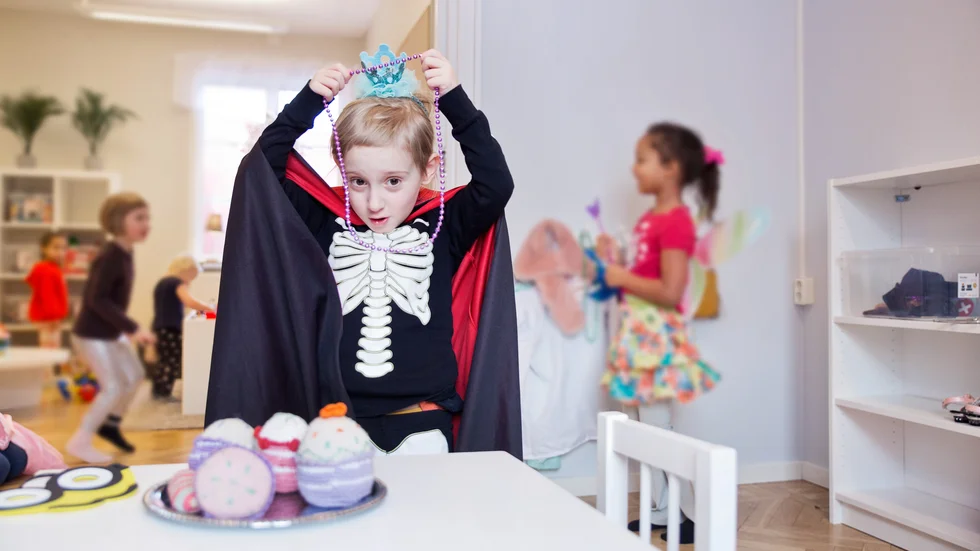 4-åriga Dag klär ut sig till ett Draculaskelett med prinsesskrona och pärlhalsband. I bakgrunden leker hans tvillingsyster Daphne med de andra kompisarna på förskolan i Kräklingbo.