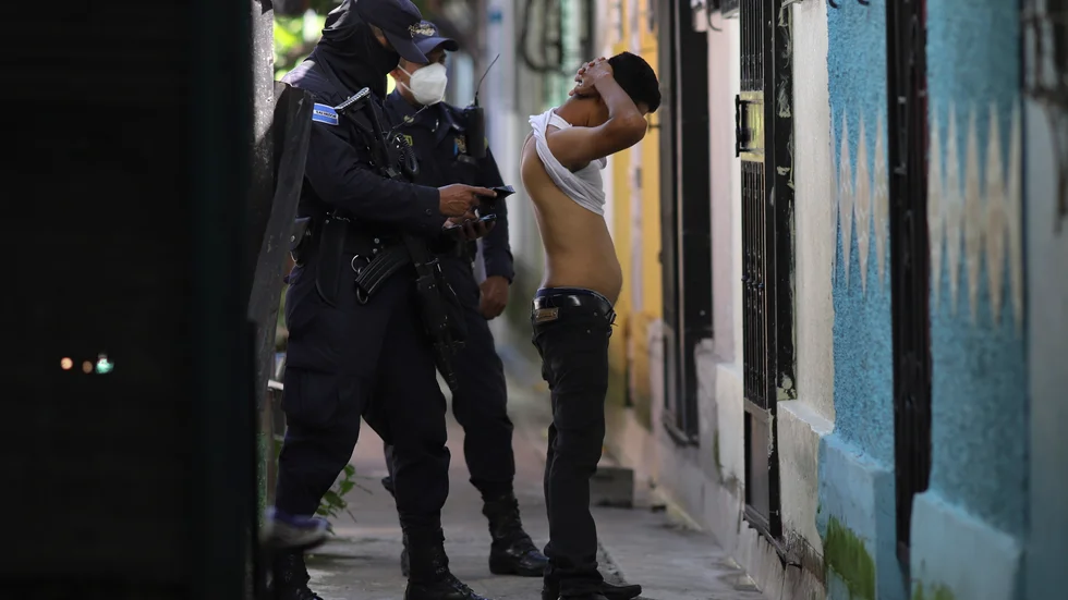 Poliser kroppsvisiterar en man under en sökinsats efter gängmedlemmar i Soyapango utanför San Salvador den 16 augusti.