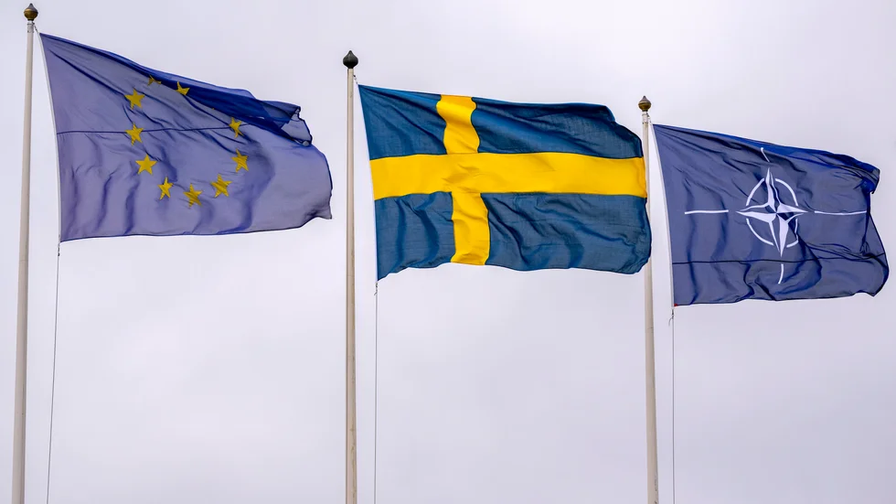 EU-flaggan och NATO-flaggan vajar på vars en sida om den svenska flaggan.