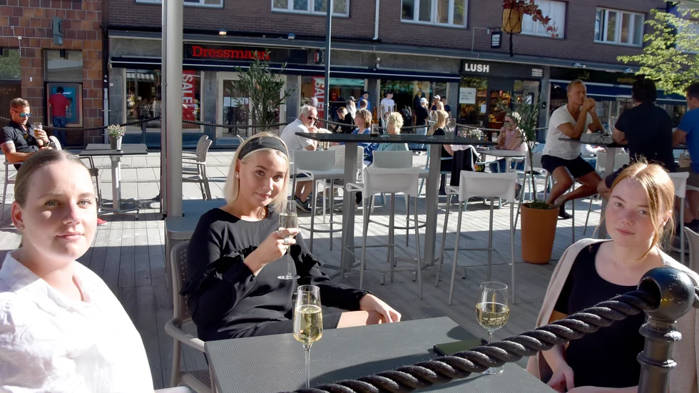 Vännerna Louise Lindström, Alva Wikström och Terese Nilsson njuter i solen på uteservering, men fortsätter att hålla distans till andra. 