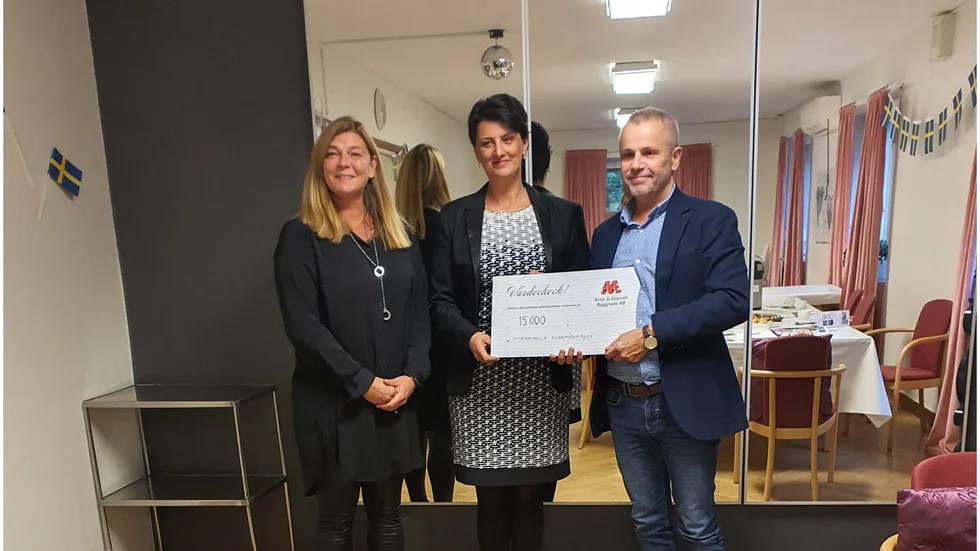 Roger Käller, vice vd för Åhlin & Ekeroth Byggnads AB, överräcker checken på 15 000 till Danijela Acimovic (mitten),ordförande i IKF Motala. Till vänster står Åsa Pettersson, redovisningsassistent på företaget.