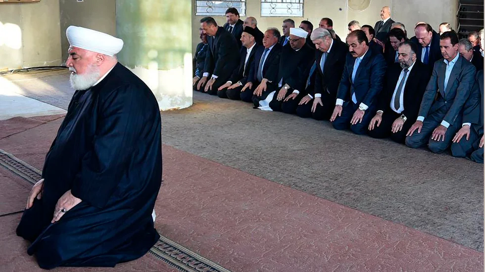 Adnan al-Afiyuni (till vänster), mufti för Damaskus-regionen, har dödats av en bilbomb. I bakgrunden syns också Syriens president Bashar al-Assad. Bild från 2016.
