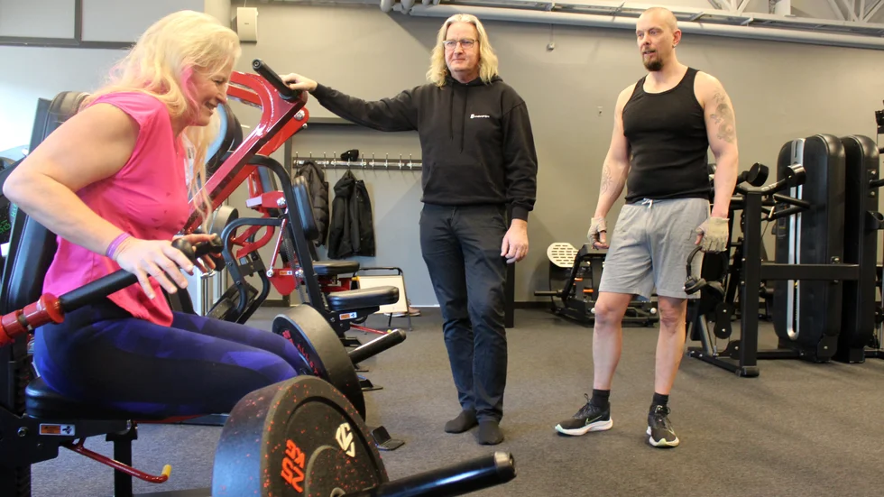 Gymvärden Ingmarie Johansson tränar i en av maskinerna under överinseende av Peter Lindberg och Adde Andersson.