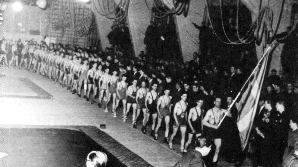 Defilering och invigning i Jägarskolans Ex-hus vid 1954 års SM i grekisk-romersk stil med fyra viktklasser. Per Luthström är fanbärare.