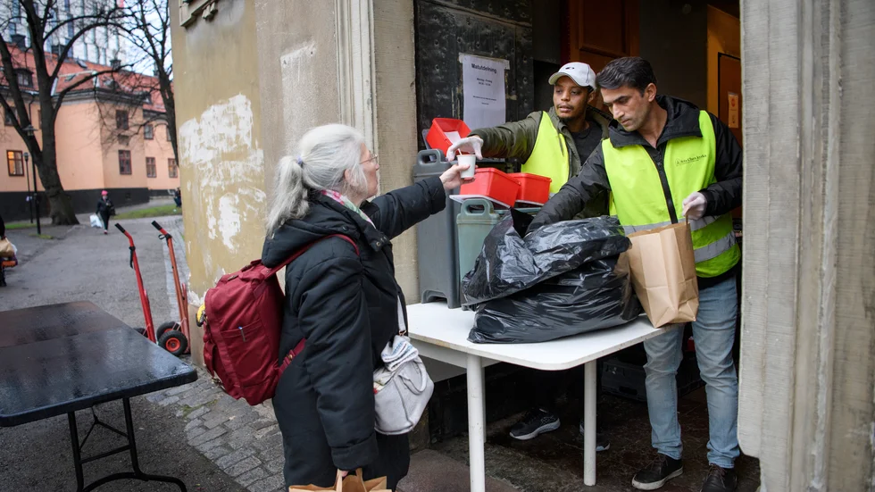 Mia Johansson får en kopp kaffe och en påse med mat av Bajo Gabrimariam och Wahid Nafipour vid St:a Clara kyrka, som delar ut mat till hemlösa.