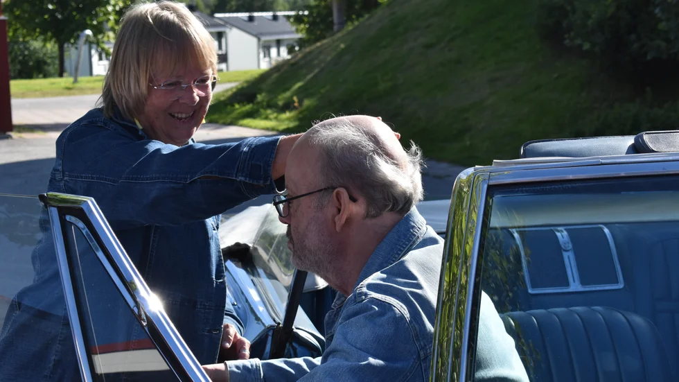 Gunn Holmbom hjälper sin man Anders "Hompa" Holmbom ner i en blå Buick. "Det här kommer gå bra".
