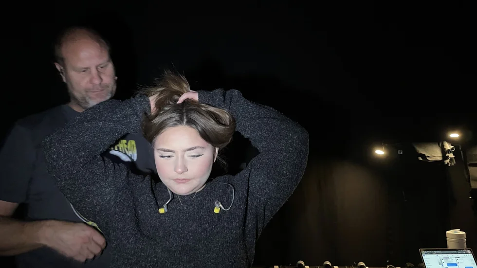 Förberedelse bakom Idolscenen. Frilansande ljudteknikern Kenneth Back hjälper Louisa med att få headsetet på plats och öronsnäckorna in i öronen. Samtidigt nynnar hon och sjunger några strofer för att sätta igång rösten. 
