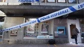 En polistekniker kliver i genom den sönderslagna dörren för att undersöka banklokalen.