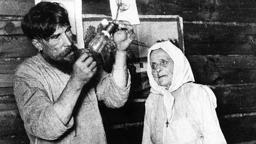 Den ryske bonden skruvar i sin första glödlampa - glödlampan kallades "Iljitj" efter Lenin - 1925, medan hustrun ser på.