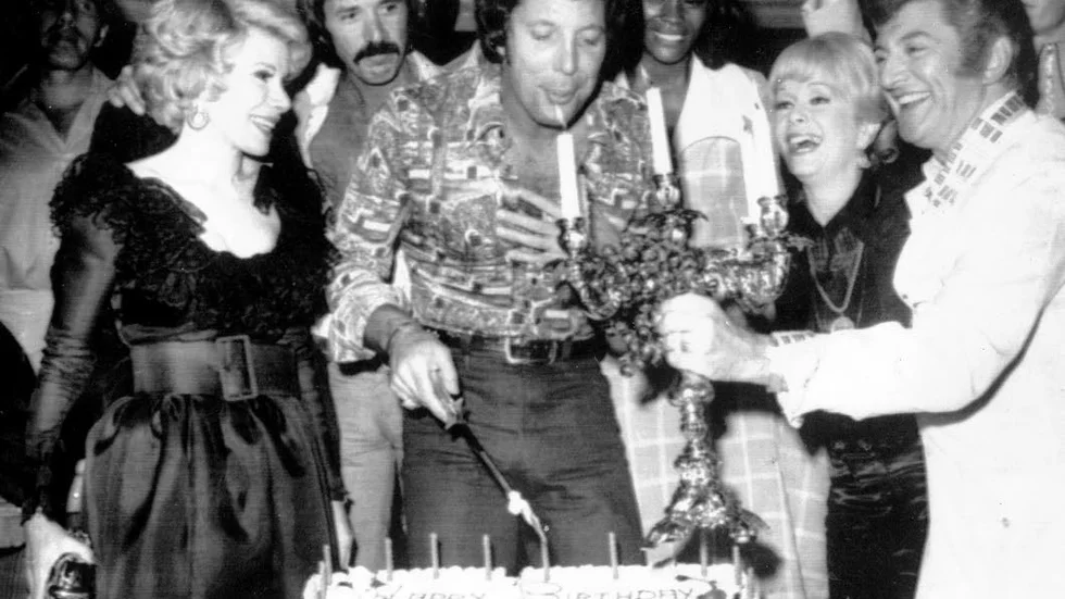 Sångarikonen Tom Jones blåser ut ljus på ett överraskningsparty på Caesar's Palace i Las Vegas, 1974. Från vänster: Joan Rivers, Sonny Bono, Tom Jones, Debbie Reynolds och Liberace.