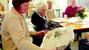 Agneta Petersson, en av tre som jobbar på dagverksamheten på Hallegården, läser tidningen. Ingrid Andersson, Ruth Persson och Inga-Britt Lundahl lyssnar uppmärksamt.