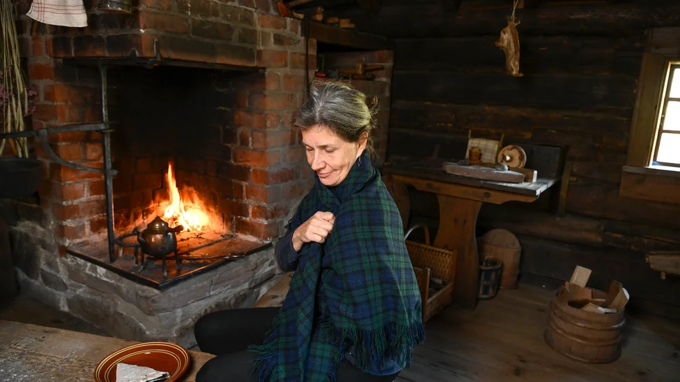 Kerstin Holm Söderkvist, museipedagog på Skansen, tänder brasan i den öppna härden i Backmats stuga på Skansen.