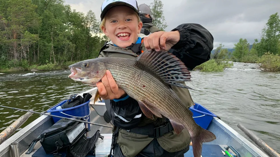 En strålande glad Rasmus Holmberg visar upp sin nyfångade harr på 0,94 kilo. Harren fick Rasmus på spinnare i Piteälven.
