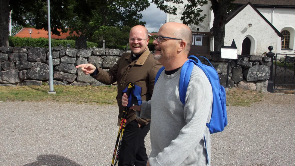 Lars Kilström, Strengnäs Tidning, diskuterar pilgrimsleden med kyrkoherden Liuus Jaehnke. I bakgrunden ses Vansö kyrka.