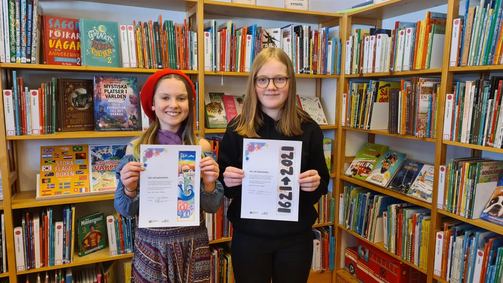 Lisa Rönnlund och Alicia Myrestam, klass 6 på Norrbyskolan i Hortlax, visar upp sina jubileumsbokmärken.